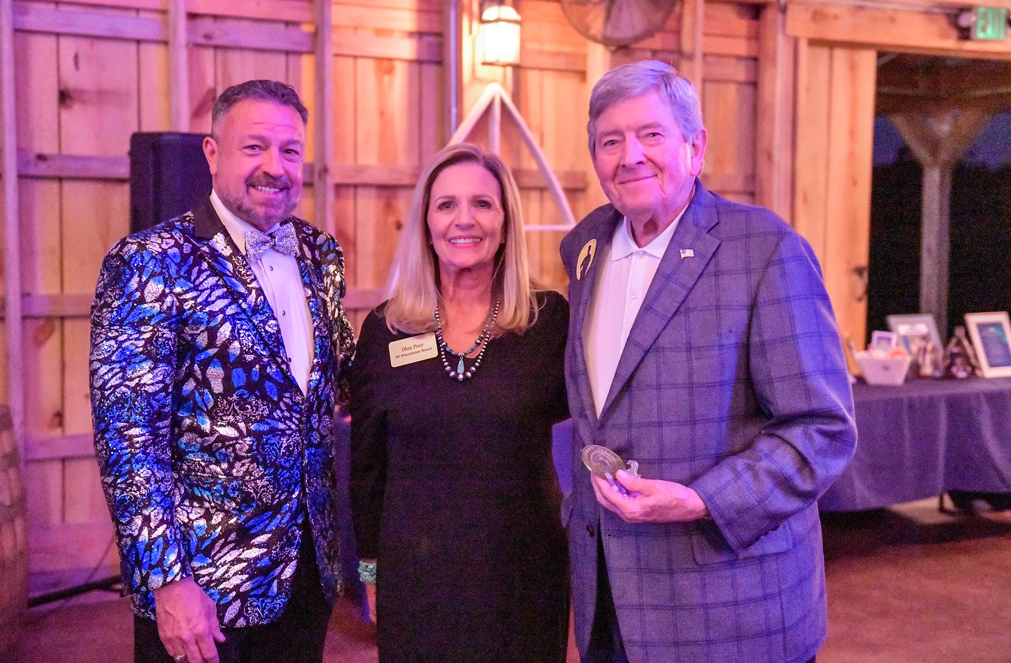 Three well dressed individuals smiling in a barn style event